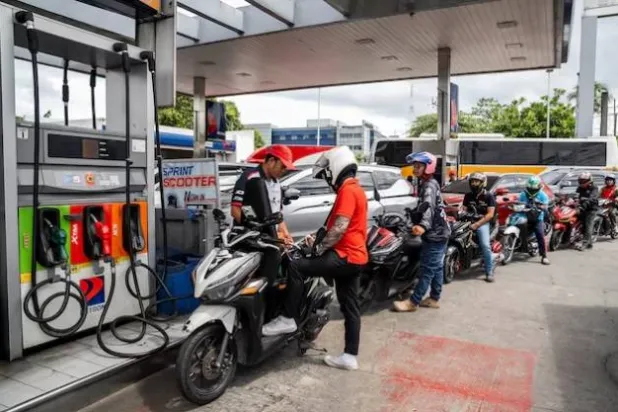 عامل يقوم بتعبئة خزان دراجة نارية بينما يصطف السائقون في محطة وقود بمدينة كويزون- مترو مانيلا (رويترز)