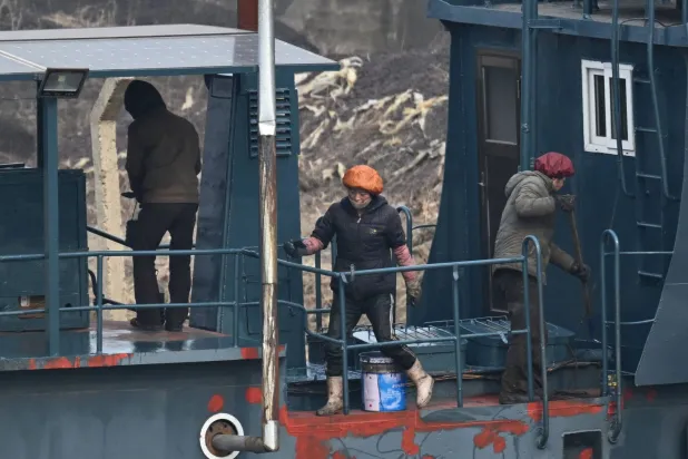 عمال كوريون شماليون يطلون قارباً على ضفة نهر يالو في بلدة سينويجو الكورية الشمالية (أ.ف.ب)