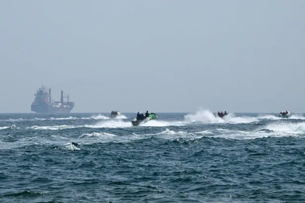 Small boats sail loaded with goods in front of a container ship in the waters of the Strait of Hormuz off the coast of Oman, June 25, 2025 (AFP)