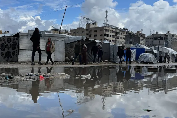 نازحون فلسطينيون يمشون إلى جانب خيامهم التي غمرتها مياه الأمطار في مدينة غزة يوم الخميس (د.ب.أ)