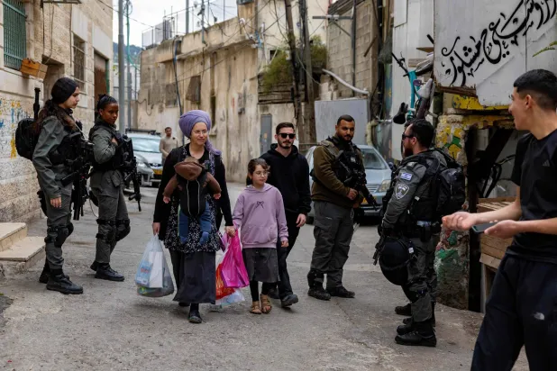 A Palestinian man (R) watch a settler family walks past a group of Israeli police officers as 11 Palestinian families in the Batan al-Hawa area of Silwan are evicted to make room for Israeli settlers, in the predominantly Arab neighbourhood of Silwan, in East Jerusalem on March 25, 2026. (Photo by Odd ANDERSEN / AFP)