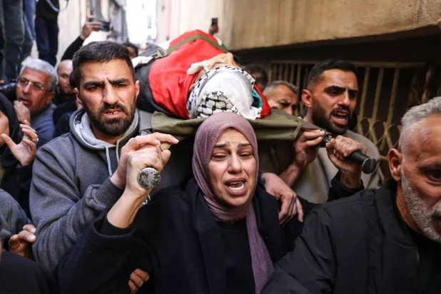 والدة الفتى آدم دهمان (15 عاماً) الذي قتله الجيش الإسرائيلي تحمل جثمانه خلال جنازته في مخيم الدهيشة ببيت لحم في الضفة الغربية المحتلة (أ.ف.ب)