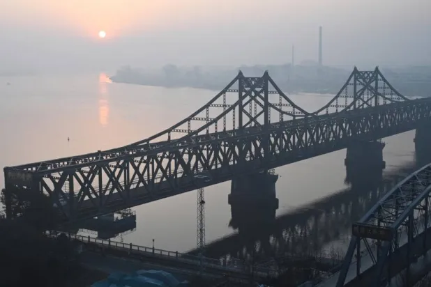 The sun rises over the North Korean town of Sinuiju, behind the Sino-Korean Friendship Bridge (L) and the Yalu River Broken Bridge (R), as seen from the border city of Dandong, in China's northeast Liaoning province on March 26, 2026. GREG BAKER / AFP
