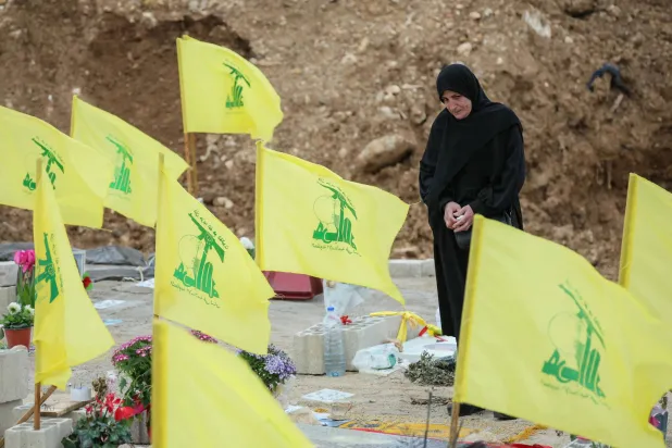 A woman stands amid Hezbollah flags on March 29, 2026, in the Choueifat area on the outskirts of Beirut during the funeral of journalists killed the previous day in an Israeli strike in south Lebanon. (AFP)