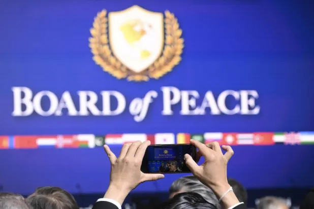 مشارك في اجتماع «مجلس السلام» لغزة يلتقط صورة للشعار خلال أول اجتماعاته بواشنطن في 19 فبراير 2026 (إ.ب.أ)