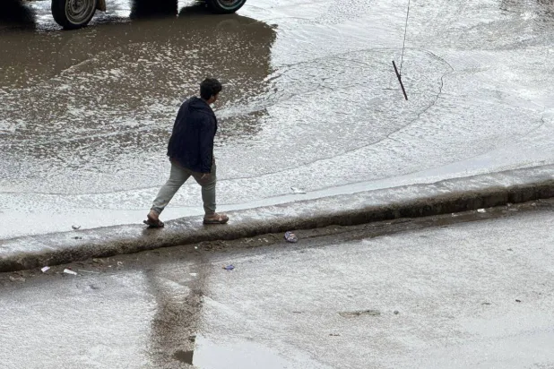 شاب مصري يسير وسط المياه في منطقة فيصل بمحافظة الجيزة بعد أن غمرت الأمطار الطرق (الشرق الأوسط) 