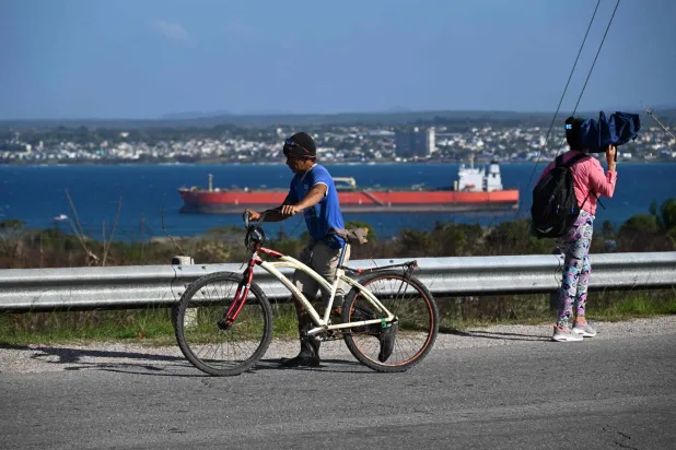 A man walks with a bike as an oil tanker ship sails on Matanzas Bay, Cuba on March 30, 2026. (Photo by Yamil LAGE / AFP)