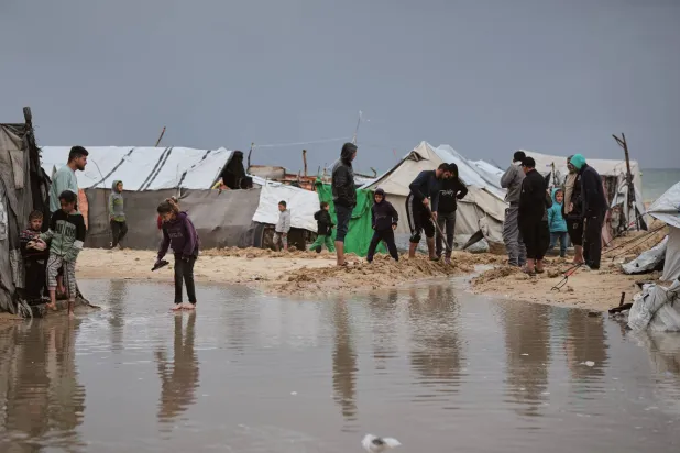 Palestinians walk through a flooded area in a temporary tent camp after heavy rainfall in Gaza City, Thursday, March 26, 2026 (AP Photo/Jehad Alshrafi)