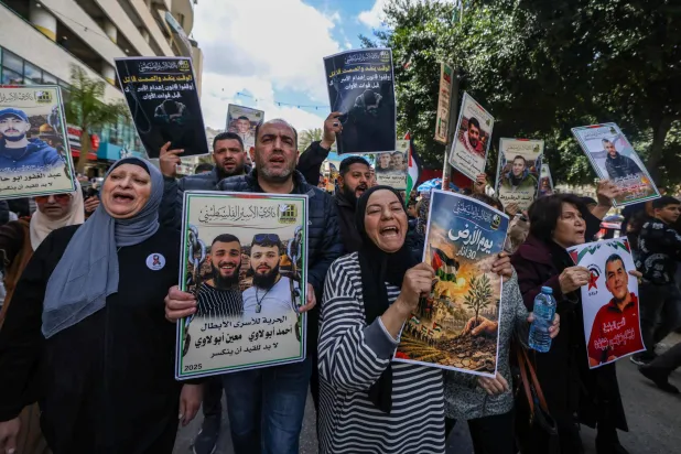 أقارب الأسرى الفلسطينيين يحملون لافتات ويهتفون بشعارات خلال مسيرة في مدينة نابلس بالضفة الغربية (أ.ف.ب)