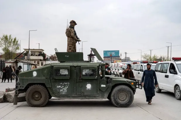 عنصر من «طالبان» يقف فوق مركبة مدرعة بينما تنقل سيارات الإسعاف توابيت ضحايا غارة جوية باكستانية في كابل (أ.ف.ب)