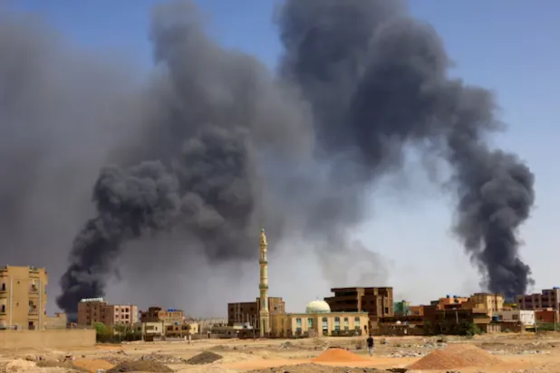 A man walks while smoke rises above buildings after aerial bombardment, during clashes between the paramilitary Rapid Support Forces and the army in Khartoum North, Sudan, May 1, 2023. REUTERS/Mohamed Nureldin Abdallah/File Photo