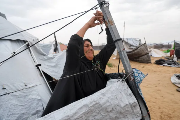 امرأة فلسطينية تشد دعائم خيمتها وسط يوم عاصف في خان يونس جنوب غزة الخميس (رويترز)