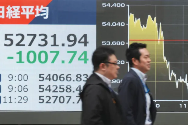 رجلان يمران أمام شاشة إلكترونية تعرض حركة الأسهم في وسط العاصمة اليابانية طوكيو (أ.ف.ب)