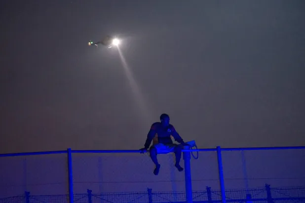 مهاجر أفريقي يحاول تسلق الجدار الفاصل بين مليلية المحتلة وإسبانيا (رويترز)