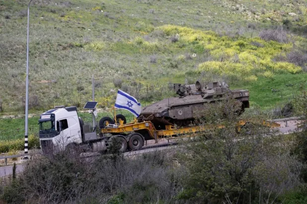An Israeli military truck transports a tank in the Upper Galilee in northern Israel near the Lebanese border (AFP) 