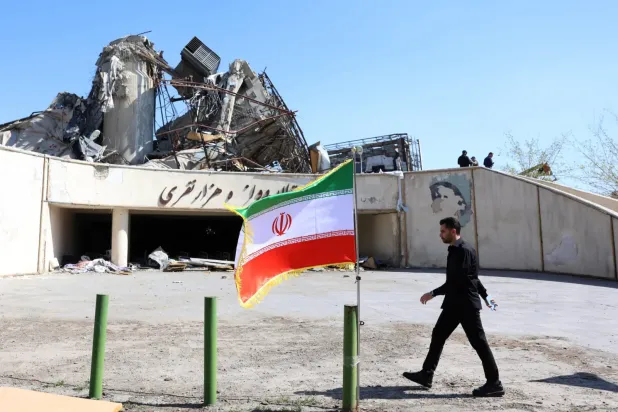 Tahran'da İran bayrağının önünden geçen bir kişi (EPA)