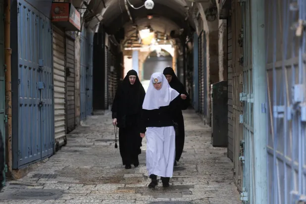 مصلون مسيحيون يسيرون بالقرب من كنيسة القيامة المغلقة بعد إلغاء موكب «أحد الشعانين» التقليدي من جبل الزيتون في البلدة القديمة بالقدس (رويترز)