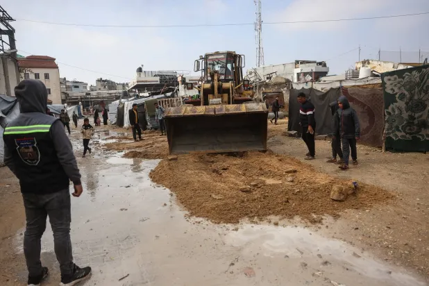 جرافة تقوم بإزالة المياه من شارع غمرته المياه في مخيم مؤقت يؤوي نازحين فلسطينيين في خان يونس (أ.ف.ب)