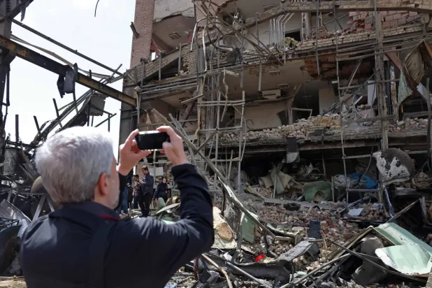 Tahran'da düzenlenen hava saldırısının ardından hasar gören Şehit Beheşti Üniversitesi binasının fotoğraflarını çeken bir adam (AFP)