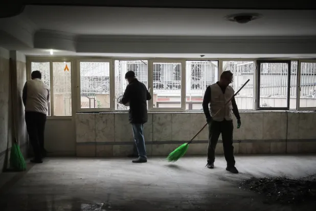رجال إيرانيون ينظفون شقة داخل مبنى سكني تعرض لغارة جوية في طهران وسط الحرب الأميركية - الإسرائيلية على إيران (د.ب.أ)