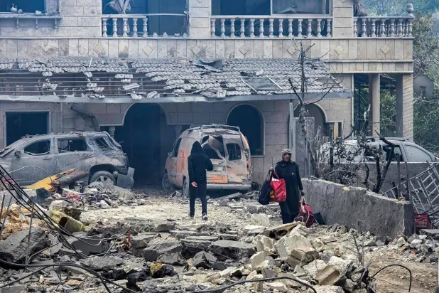 امرأة تسير حاملة ما أمكن إنقاذه من مقتنياتها بين أنقاض مبنى دمّرته غارات إسرائيلية ليلية على بلدة معركة في جنوب لبنان (أ.ف.ب)