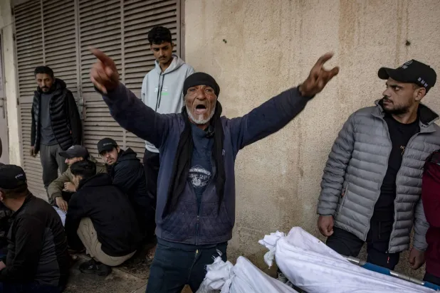 فلسطينيون بجوار جثامين ضحايا غارة جوية إسرائيلية في وسط قطاع غزة يوم الثلاثاء (إ.ب.أ)