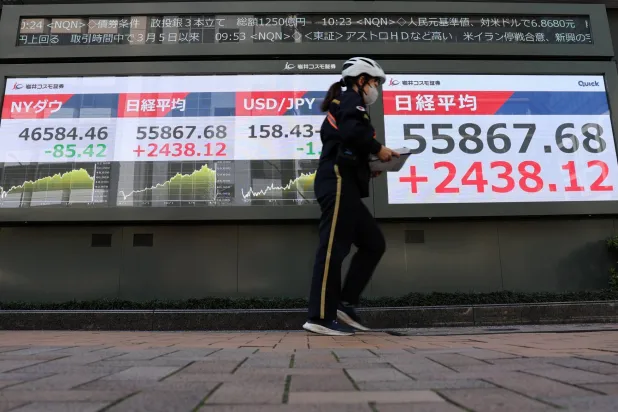 ساعية بريد تمر أمام شاشة تعرض حركة الأسهم في طوكيو (رويترز)