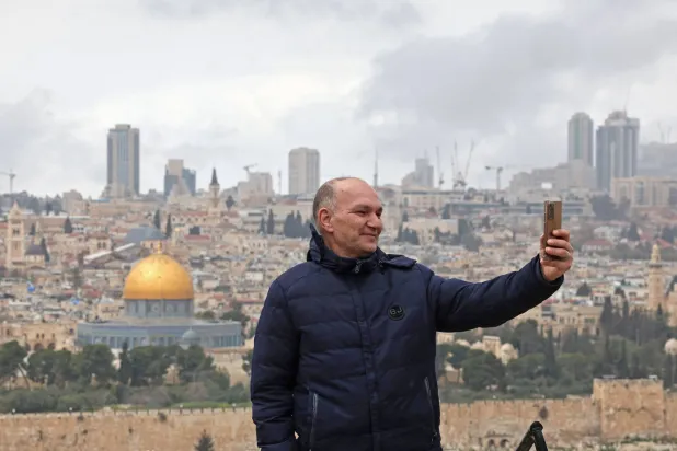 فلسطيني يلتقط صورة سيلفي مع المسجد الأقصى يوم الأربعاء الذي ظل مغلقاً منذ بدء الحرب (أ.ف.ب)