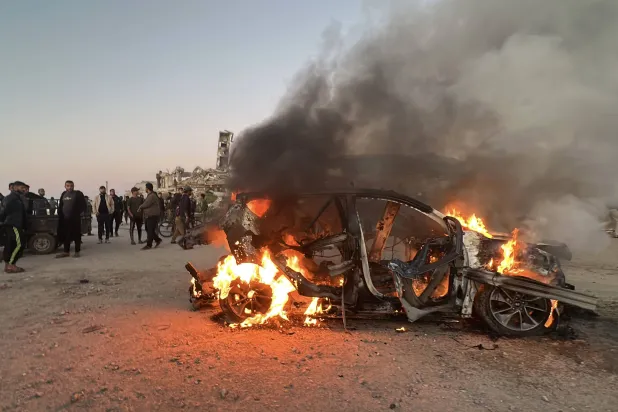 يقف الناس قرب سيارة محترقة عقب غارة إسرائيلية أسفرت عن مقتل في قناة الجزيرة (د.ب.أ)