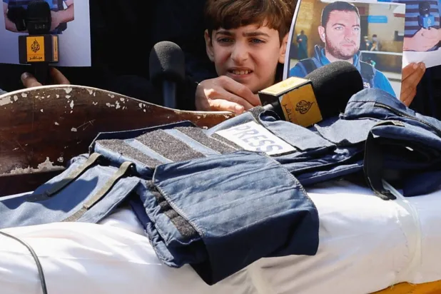 ينظر ابن الصحافي محمد وشاح نحو سترة وميكروفون موضوعين على جثمان والده خلال جنازته في مستشفى شهداء الأقصى بدير البلح (رويترز)