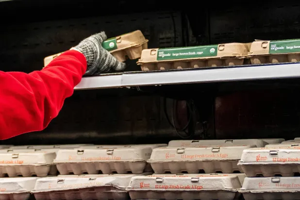 عامل يرتّب البيض على رف داخل سوبر ماركت في نيويورك (رويترز)