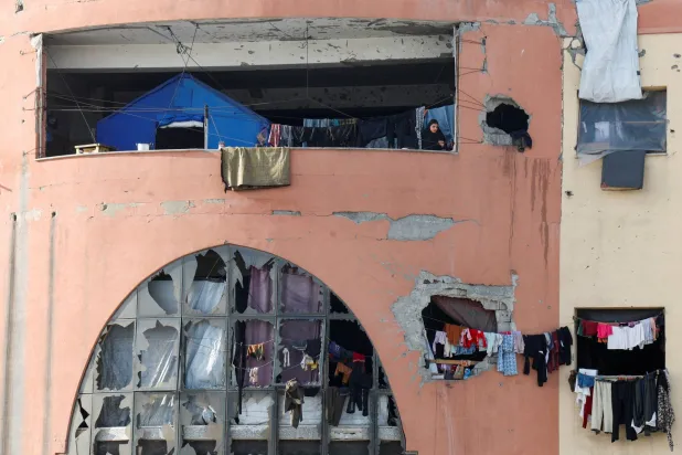 امرأة فلسطينية نازحة تقف على شرفة داخل مبنى مهدم في جامعة الأقصى جنوب غزة يُستخدم كمأوى (رويترز)