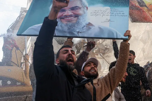 مناصرون لـ«حزب الله» يرفعون صورة لأمين عام الحزب السابق حسن نصر الله في الضاحية الجنوبية لبيروت حيث الدمار يعم المكان (رويترز)