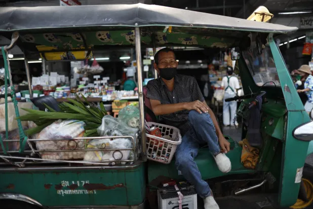 سائق توك توك وهي مركبة أجرة ثلاثية العجلات ينتظر ركاباً يشترون الطعام في سوق ببانكوك (إ.ب.أ)