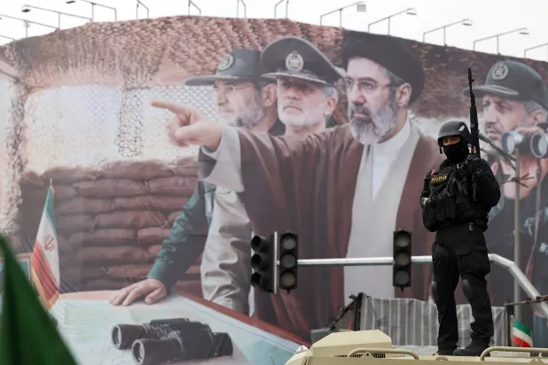 جندي إيراني يقف أمام لوحة دعائية في طهران وتظهر المرشد الجديد مجتبى خامنئي وقادة عسكريين بينهم علي رضا تنغسيري قائد بحرية «الحرس الثوري» قبل مقتله في بندر عباس (إ.ب.أ)