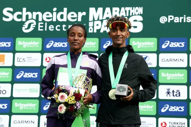 Athletics - Paris Marathon - Paris, France - April 12, 2026 Italy's Yemaneberhan Crippa and Ethiopia's Shure Demise celebrate on the podium after winning the men's and women's elite race respectively REUTERS/Tom Nicholson