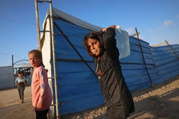 فتاة فلسطينية تحمل وعاء ماء في مخيم للنازحين بخان يونس جنوب غزة (أ.ف.ب)