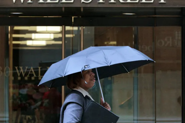 امرأة تسير تحت المطر في شارع «وول ستريت» بنيويورك (رويترز)