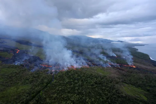 An aerial picture shows smoke rising as lava from the Piton de la Fournaise volcano  comes to a halt in Saint-Philippe, on the French Indian ocean island of Reunion, on April 2, 2026. (Photo by Richard BOUHET / AFP)