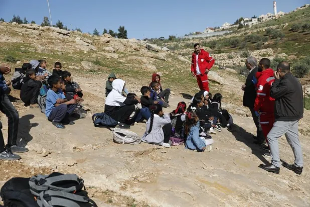  13 April 2026, Palestinian Territories, Hebron: Members of Red Crescent surround Palestinian children from Khirbet Umm al-Khair after Israeli settlers blocked the only road to their schools. (dpa)
