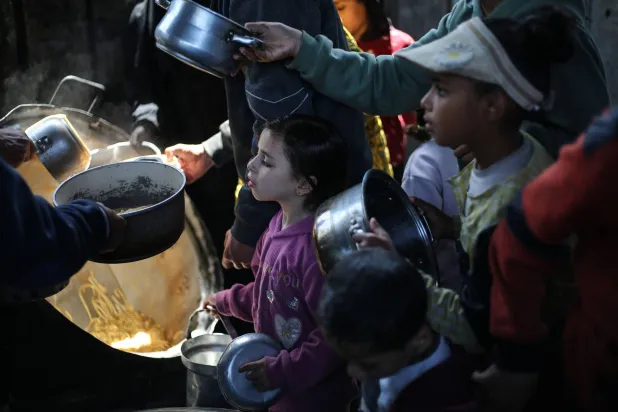 أطفال فلسطينيون نازحون يتلقون الطعام من مطبخ خيري في مخيم النصيرات للاجئين وسط غزة يوم الاثنين (أ.ف.ب)
