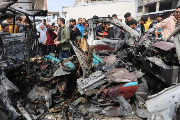 فلسطينيون يتجمعون حول حطام سيارة الشرطة التي دُمرت في الغارة الإسرائيلية (أ.ف.ب)