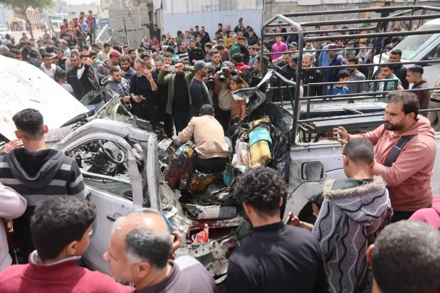 فلسطينيون في موقع حطام سيارة شرطة دمرتها غارة إسرائيلية في مدينة غزة يوم الثلاثاء (أ.ف.ب)