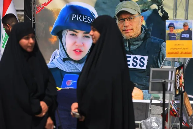 أشخاص يمرون أمام لافتة تعرض صور الصحافييَن فاطمة فتوني وعلي شعيب اللذين قُتلا في غارة إسرائيلية في جنوب لبنان خلال مظاهرة في بغداد 7 أبريل 2026 (أ.ف.ب)