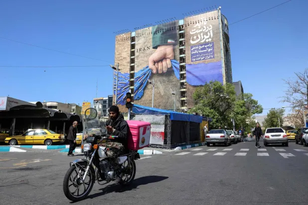 A man rides past a large billboard referring to the Strait of Hormuz in Tehran's Vanak Square on April 15, 2026. (AFP)