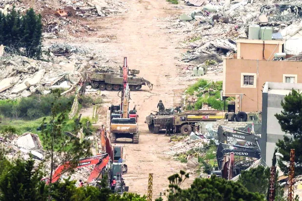 مركبات ومدرعات عسكرية إسرائيلية أمام مبانٍ مدمرة في جنوب لبنان (أ.ف.ب)