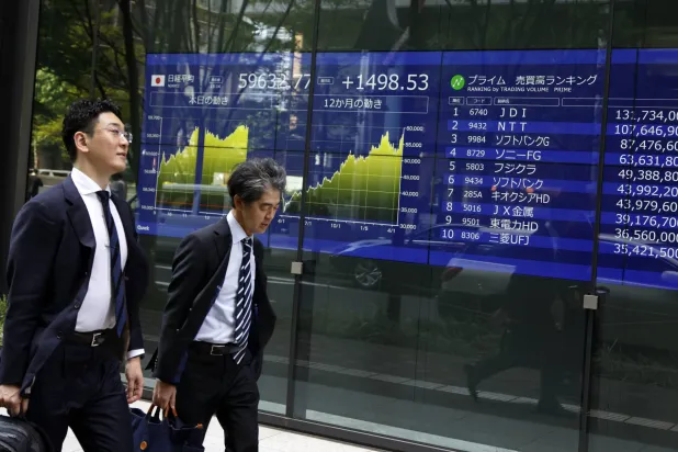 رجلان يمران أمام شاشة تعرض حركة الأسهم والعملات في العاصمة اليابانية طوكيو (إ.ب.أ)