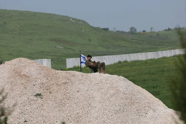 جندي إسرائيلي بجوار العلم الإسرائيلي قرب الحاجز الأمني ​​بين إسرائيل ولبنان بالقرب من أفيفيم شمال إسرائيل (إ.ب.أ)