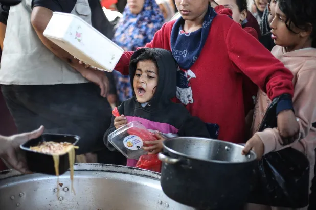 أطفال فلسطينيون نازحون يتلقون الطعام من مطبخ خيري في مخيم النصيرات للاجئين (أ.ف.ب) 
