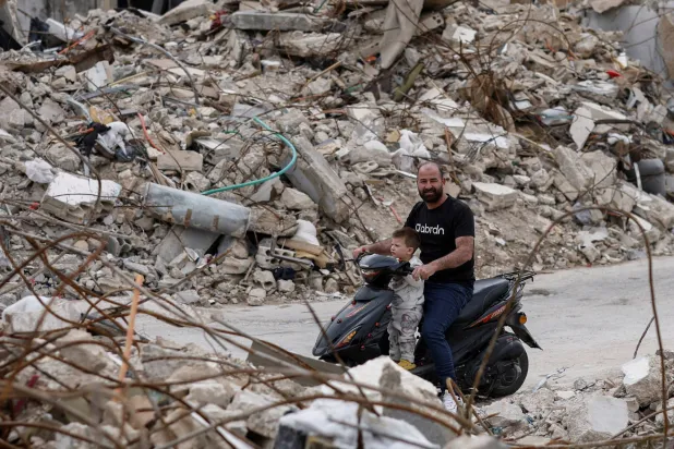 رجل وطفله ينظران إلى أنقاض المنازل التي دمرتها الغارات الإسرائيلية في جنوب لبنان (رويترز)